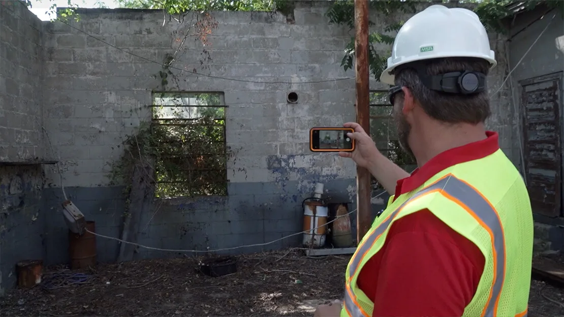 Man in hard hat and safety vest photographs deteriorated industrial room with peeling paint and debris