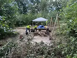 A group of geologists working in a forest with a blue tent in the background